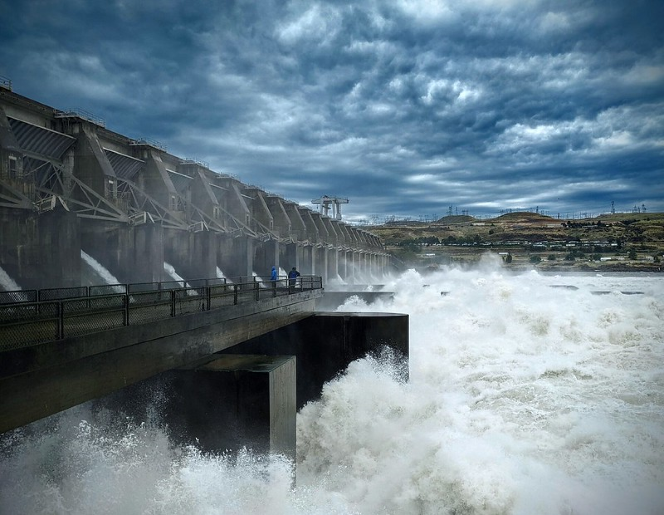 Water exits a dam’s spillway that stretches the length of a waterway.