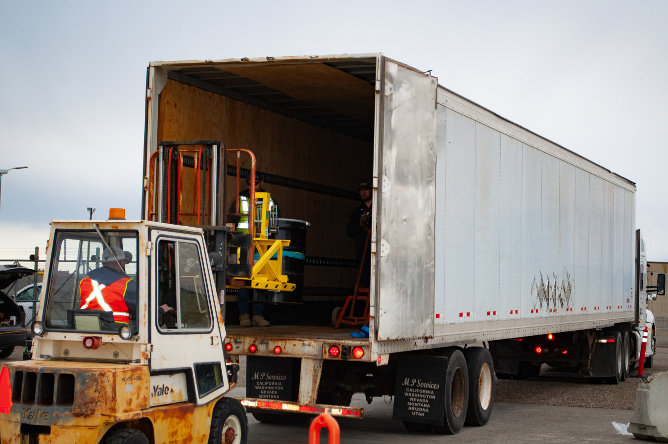 employees loading drums of waste into the back of a large truck