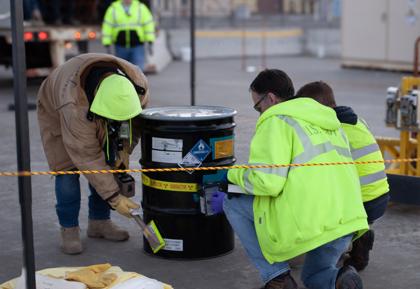 Three workers surveying the outside of a drum filled with waste