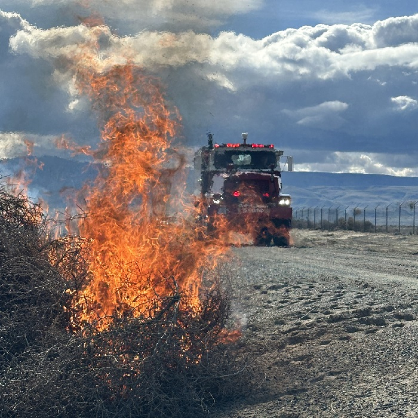 A pile of burning brush with a firetruck parked behind it 