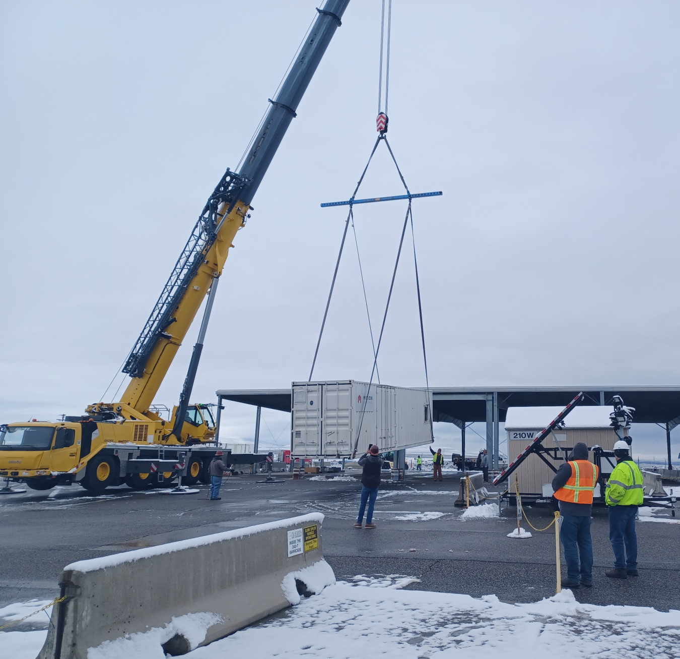 A crane loading a large white container onto a truck for disposal