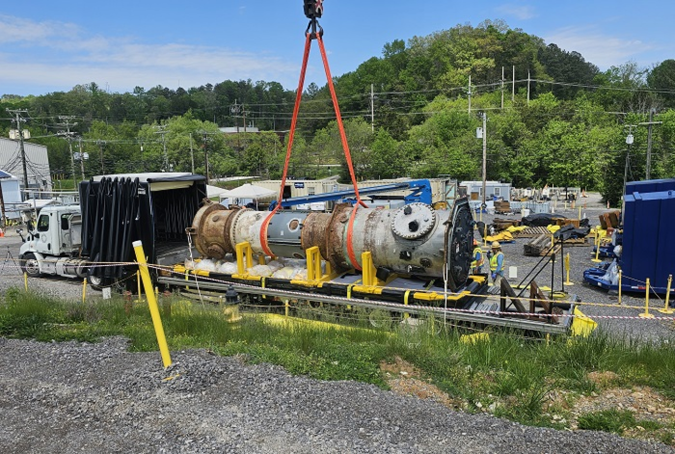 A crane loading a large cylinder container onto a large truck