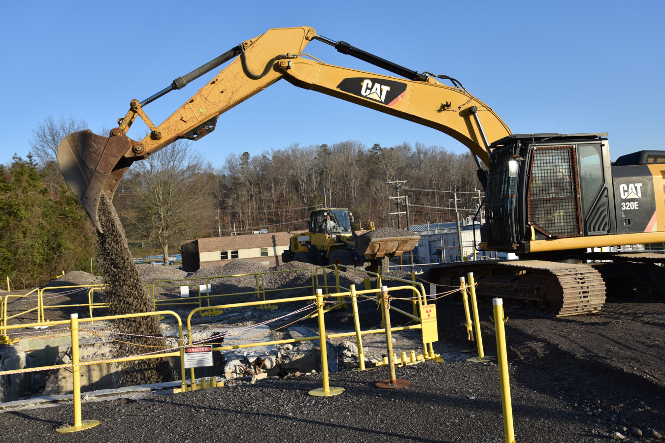 A large, yellow, construction vehicle filling a pit with dirt