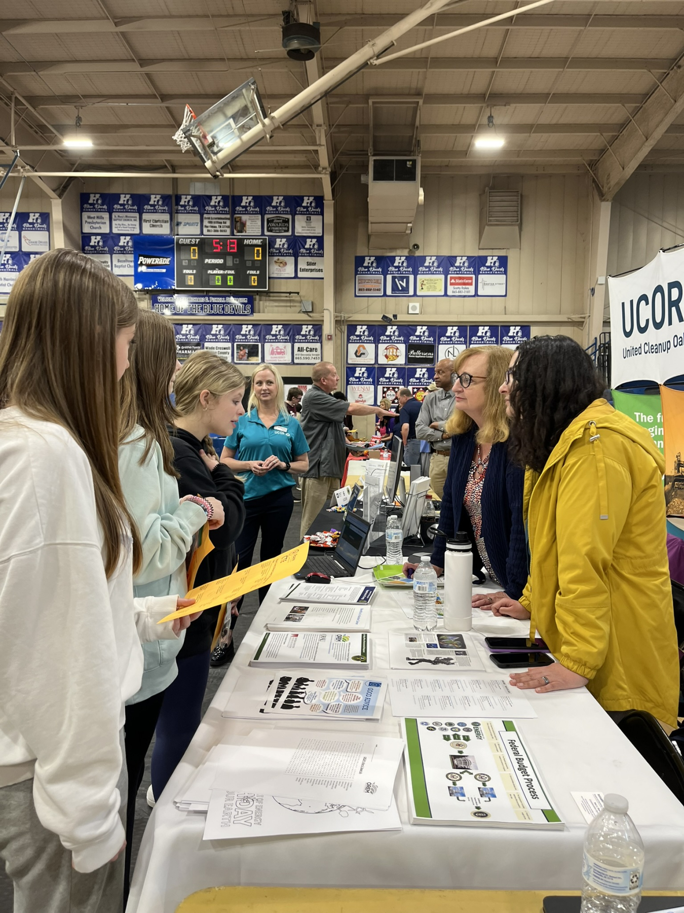 A career fair table with professionals one side and students on the other speaking to eachother
