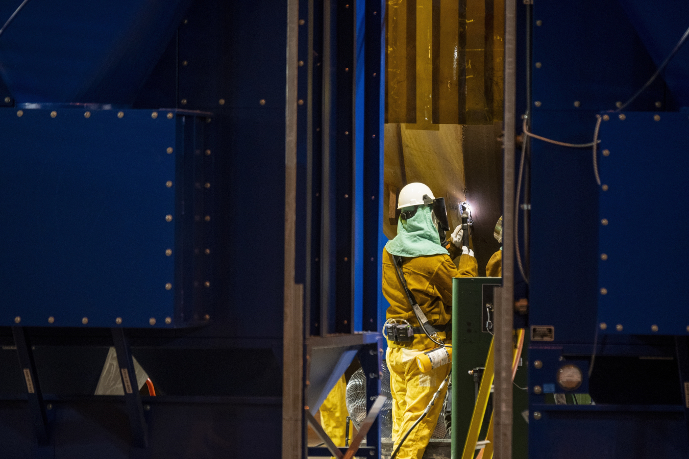 An employee in a yellow safety suit working inside of a work facility meeting 