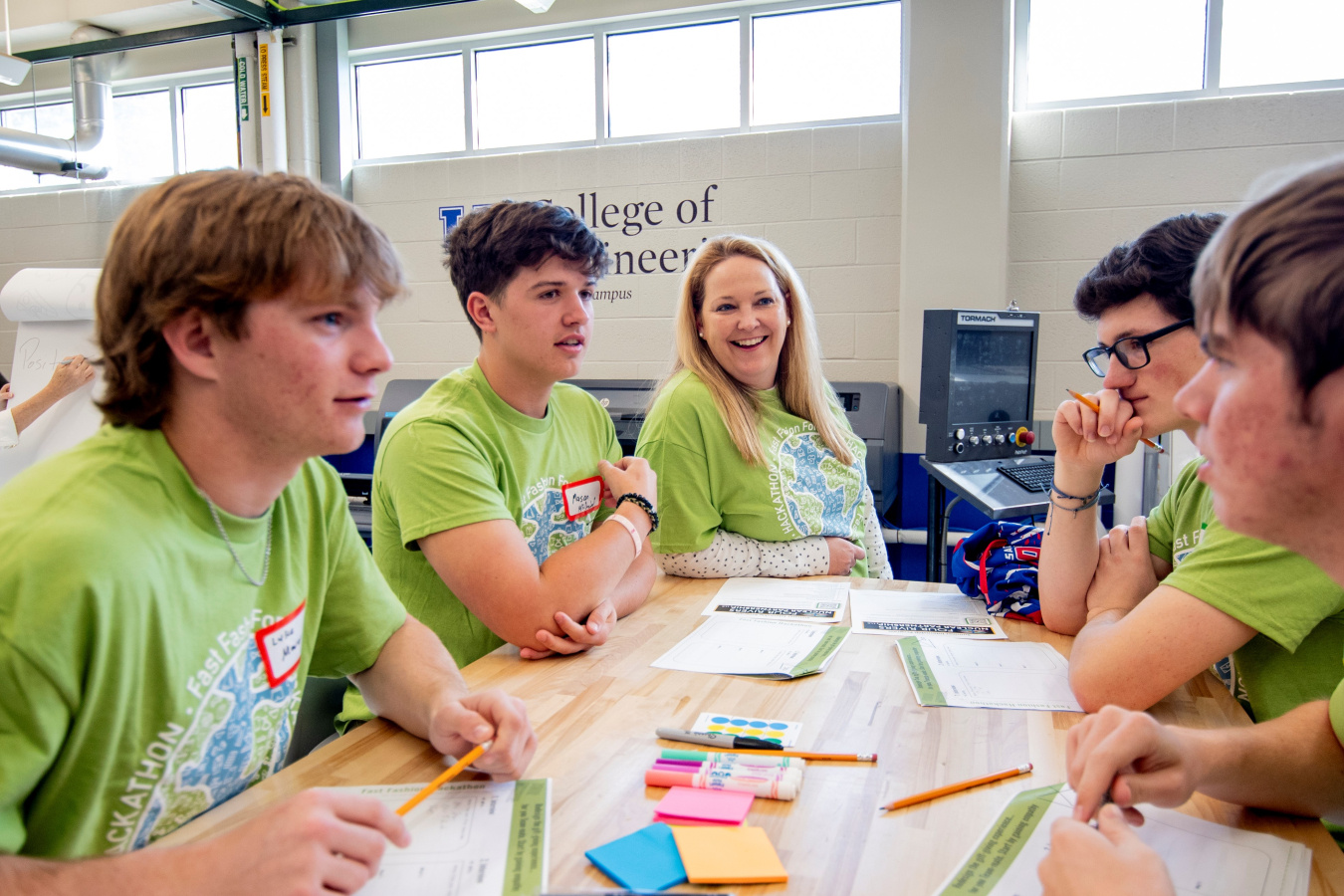 Five high school students in bright green shirts sit and talk at a table