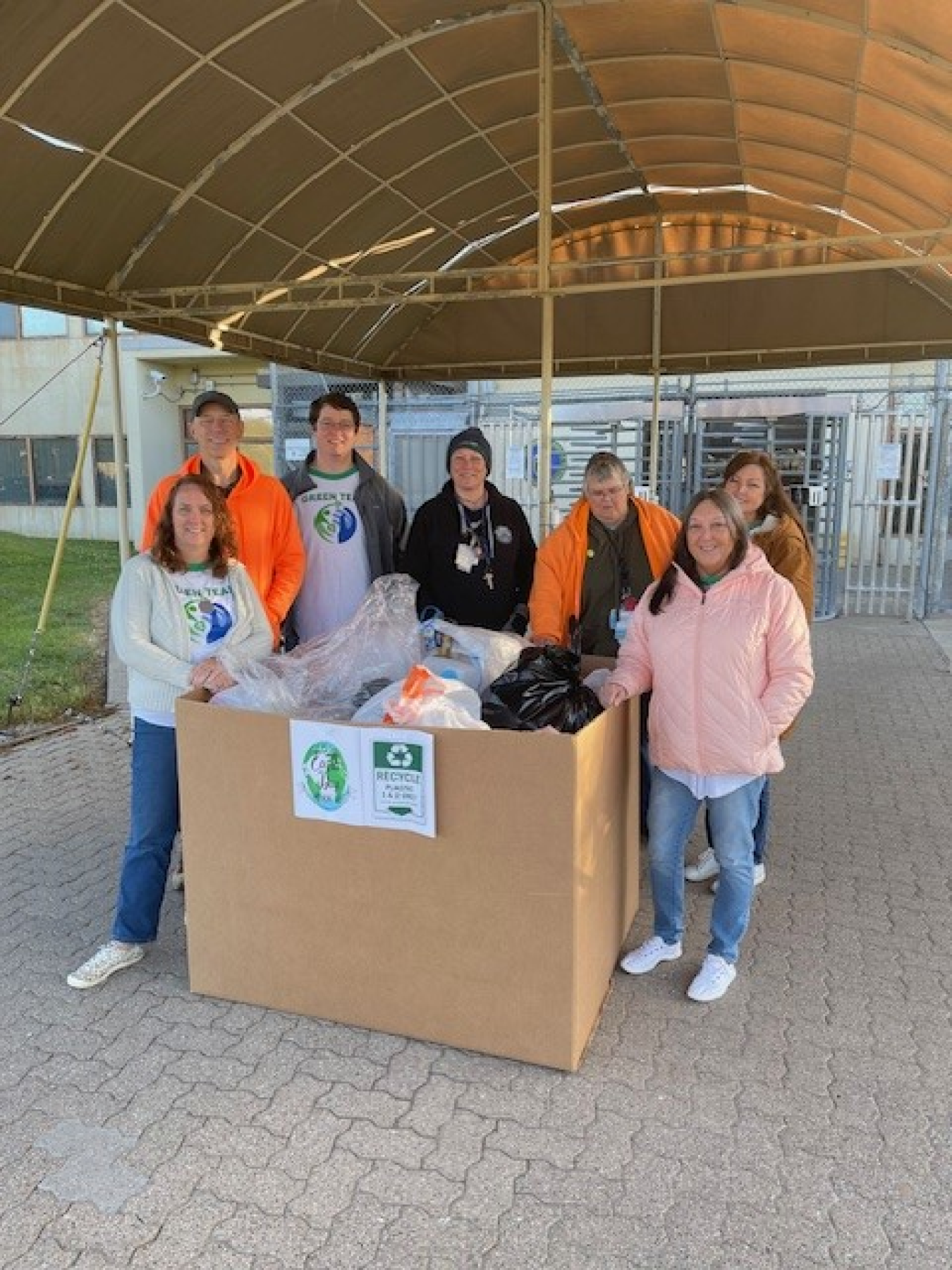 A group of people pose for a picture in front of a cardboard box filled with recycled plastic