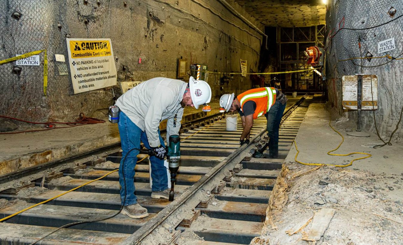 Men in hard hats using tools to disassemble an underground railing 