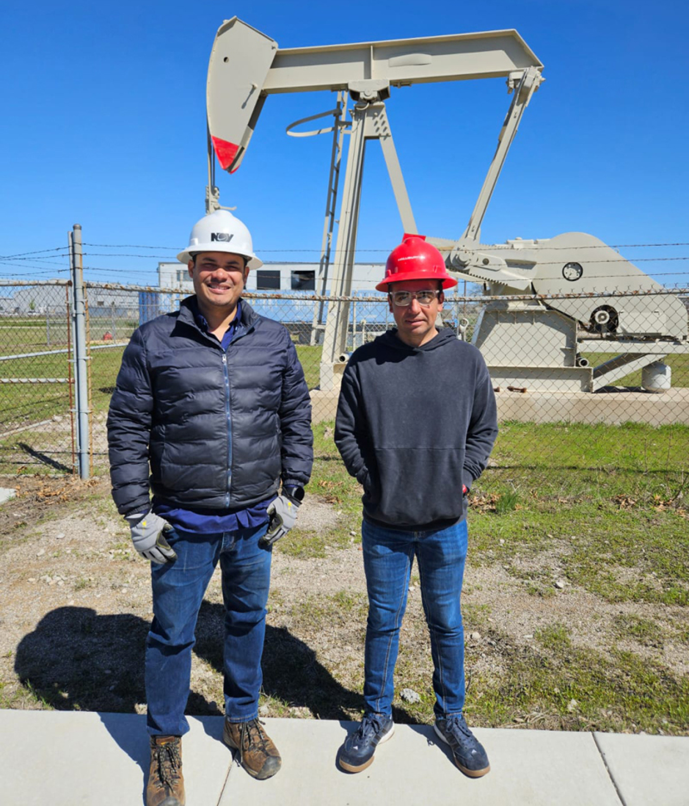 Two men standing in hard hats next to an oil rig model
