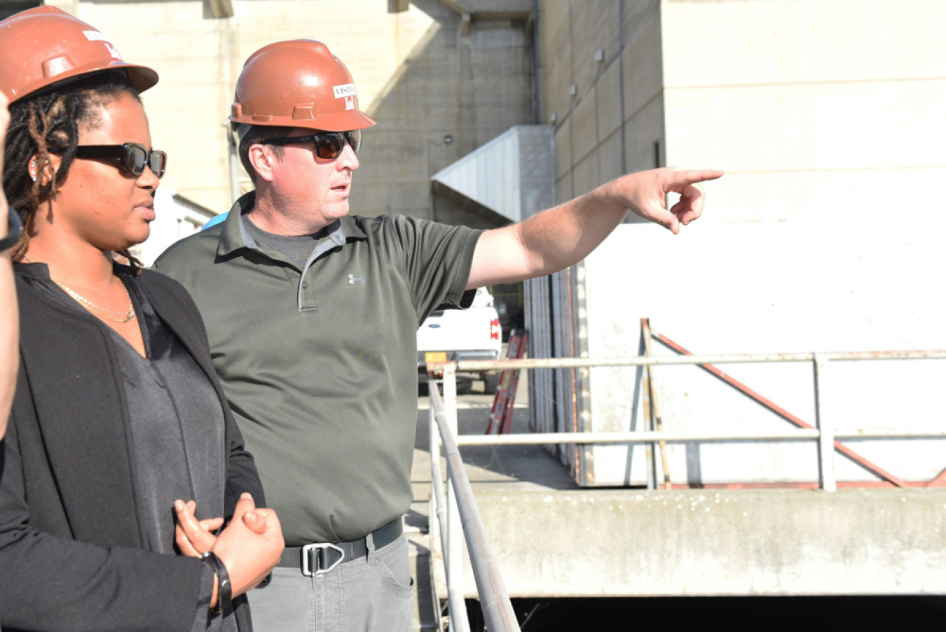 Two people stand beside each other and one is pointing out something in the distance.