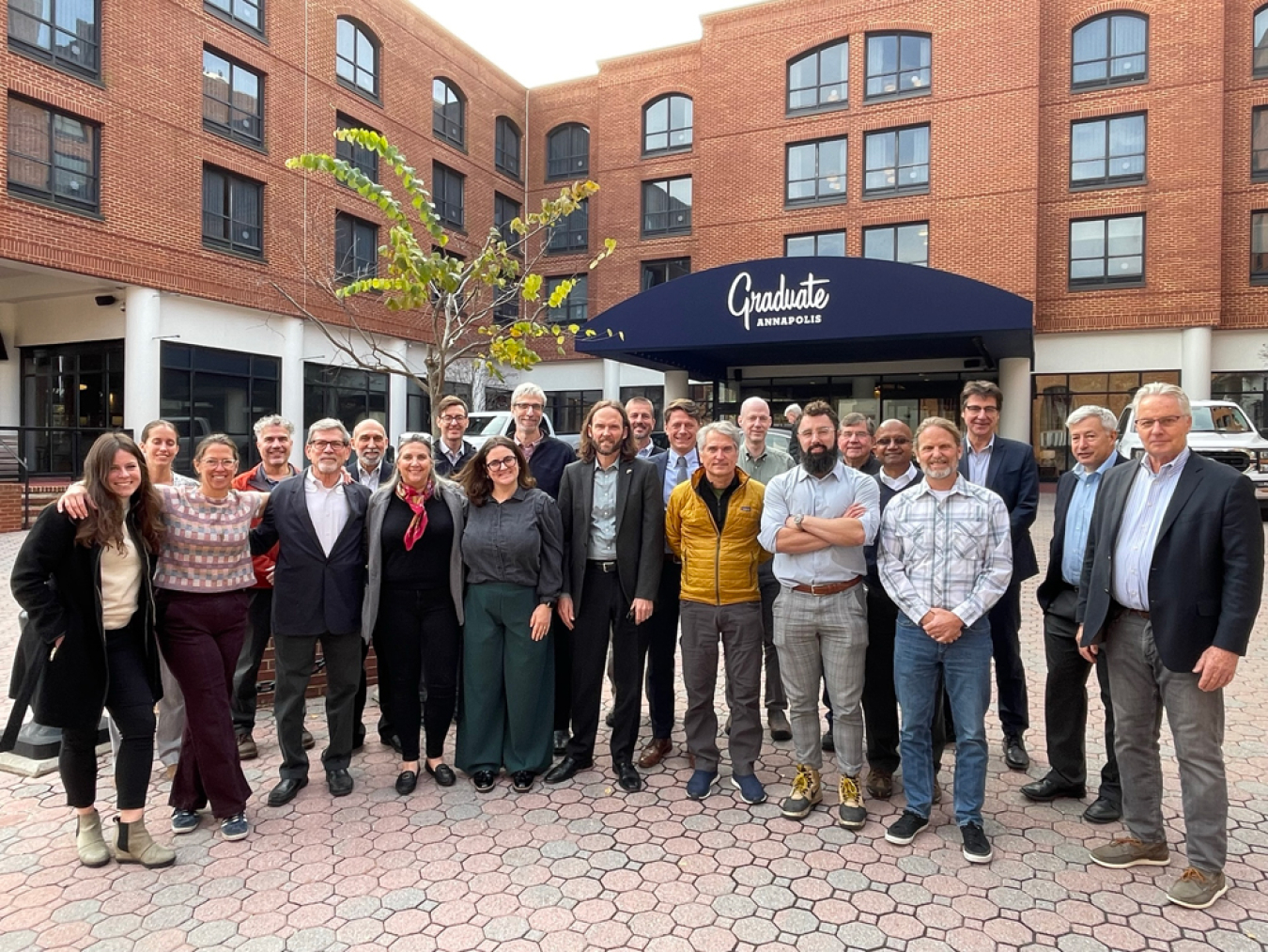 A group of people standing together in front of the exterior of a hotel/meeting building.