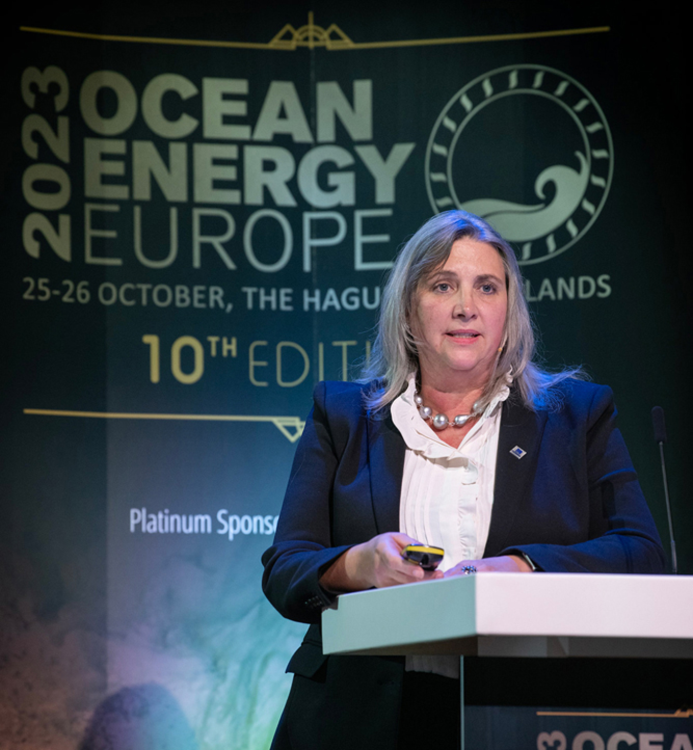 A woman stands at a podium with a sign behind her that says, in part, “2023 Ocean Energy Europe.”