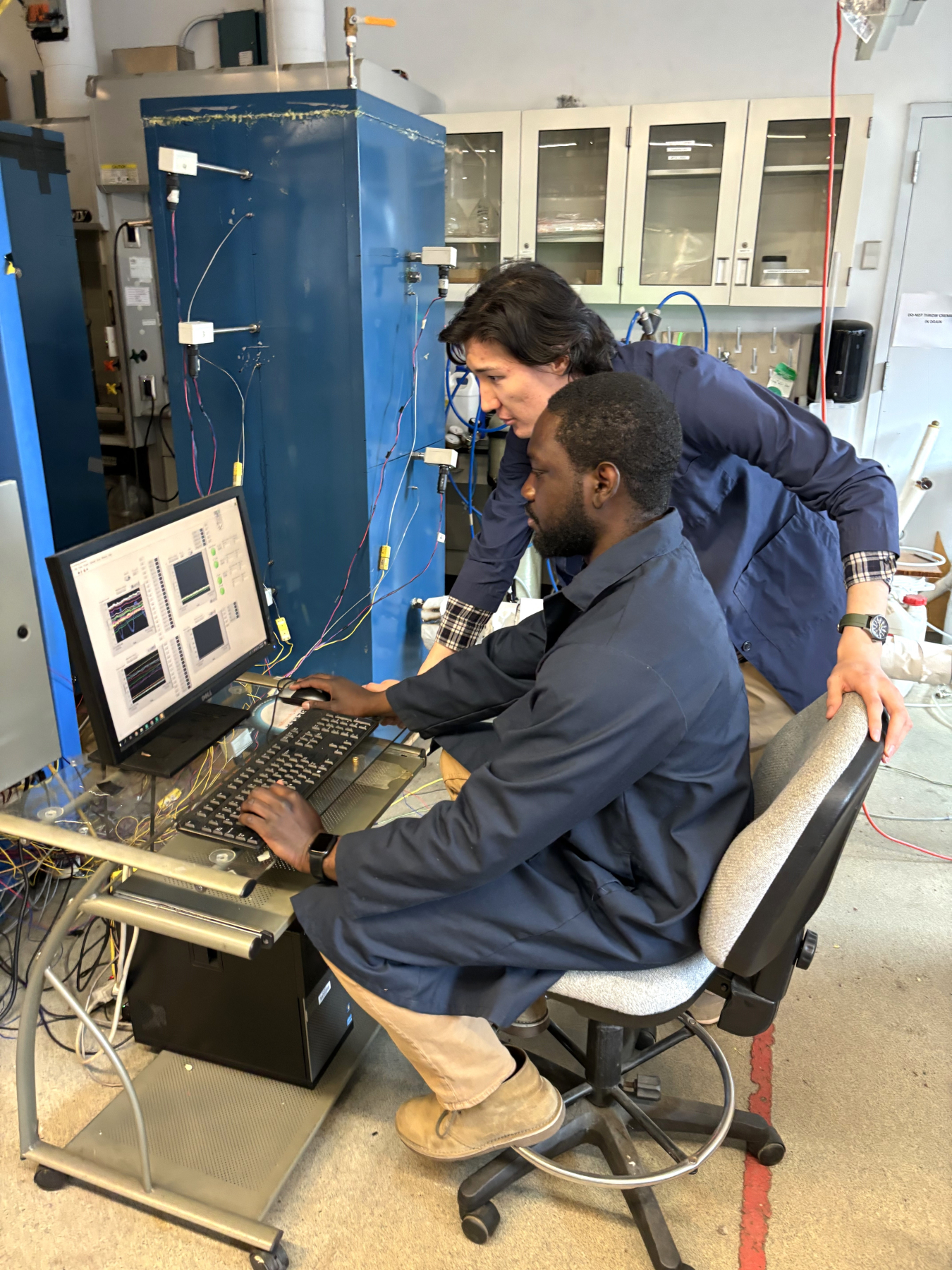 two men in dark blue jackets look at computer screen