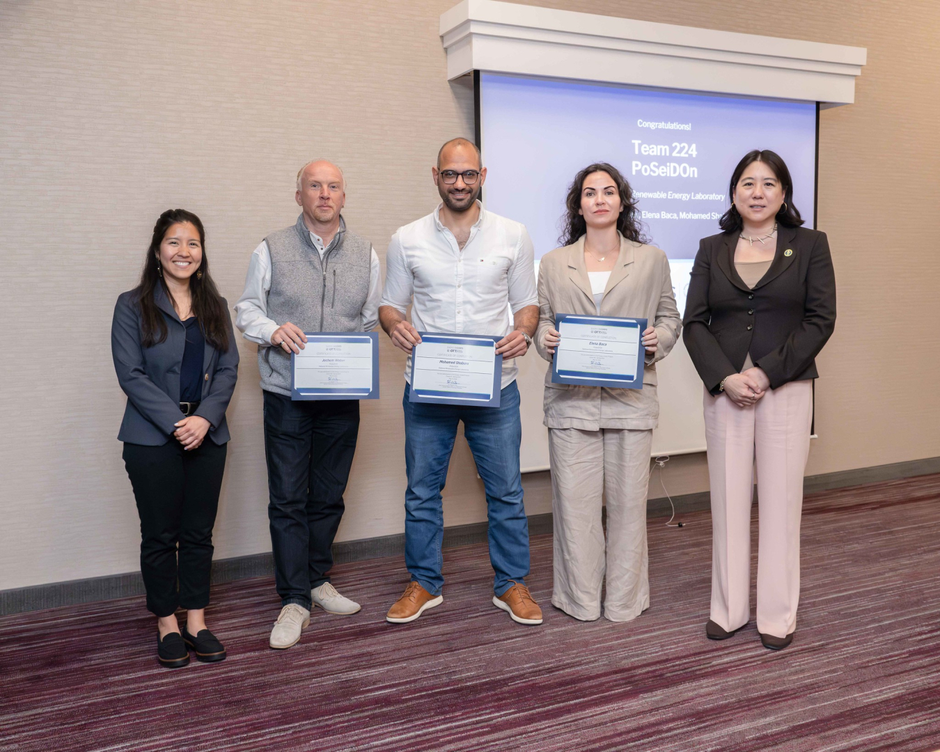 A group of five people pose and smile for the camera, with three holding certificates. 
