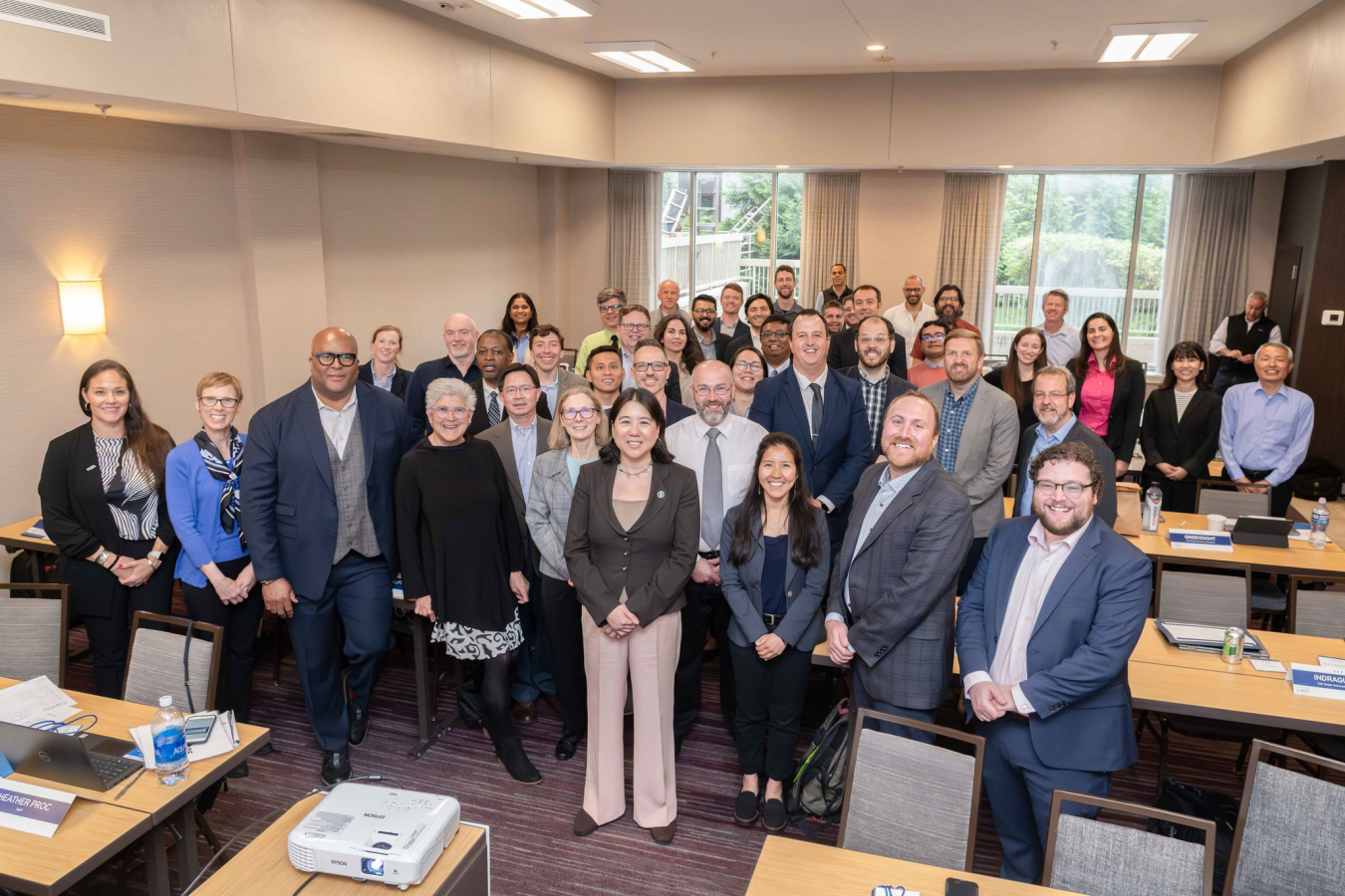 A group of 40 people pose and smile for the camera in a meeting room.