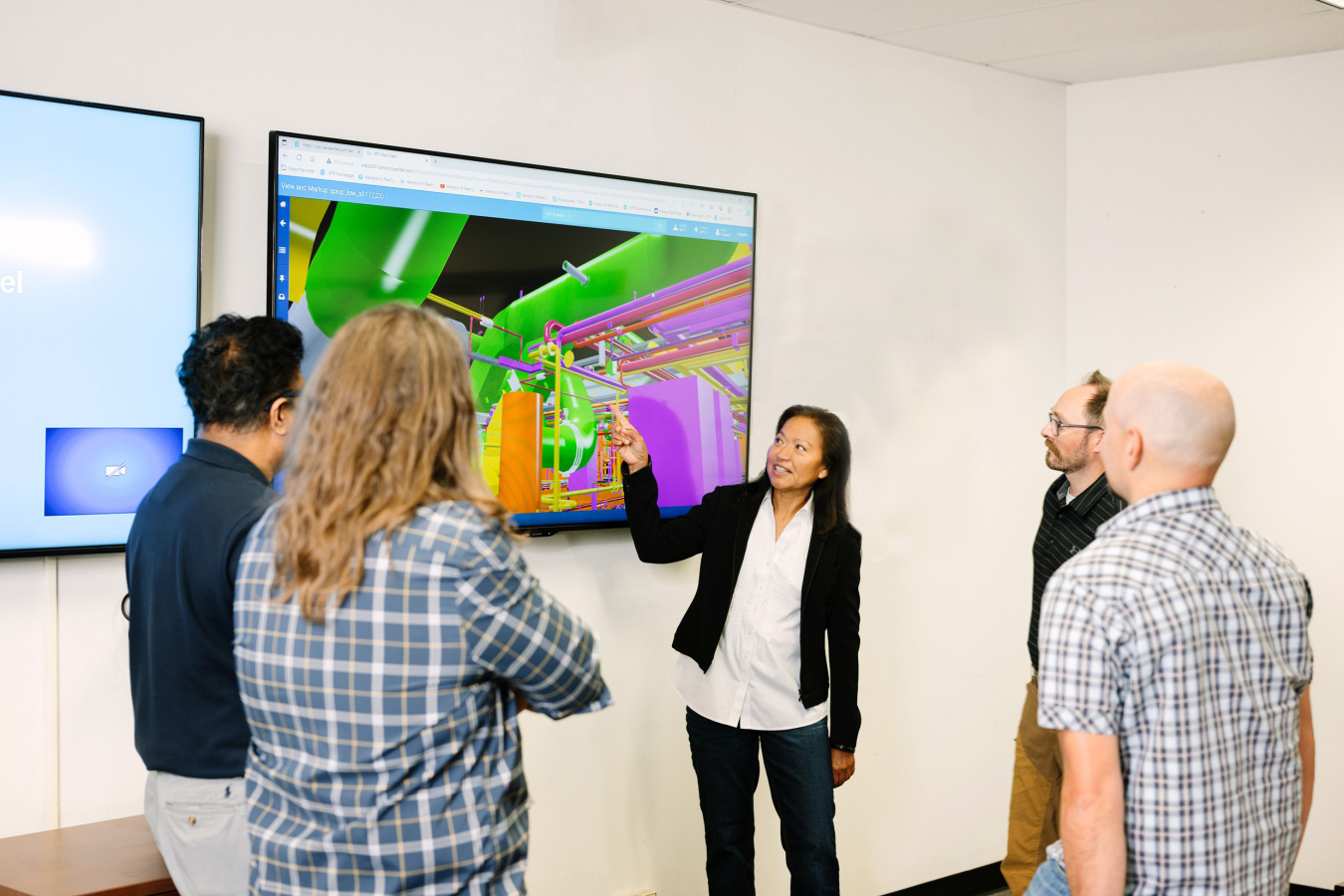 A group of people stand around a TV with a presentation on it, one woman points to the presentation 