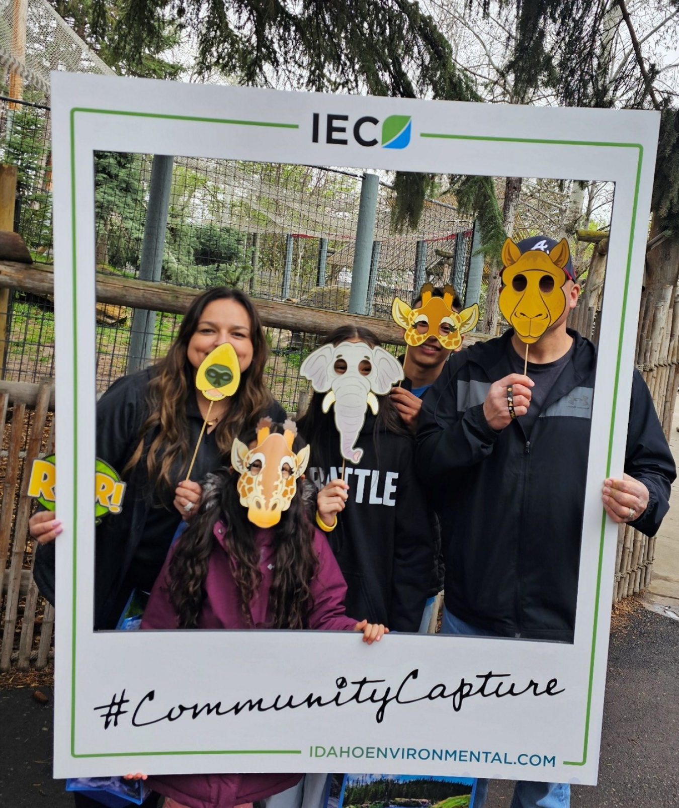 A family poses inside an oversized picture frame and hold animal face masks up to their face