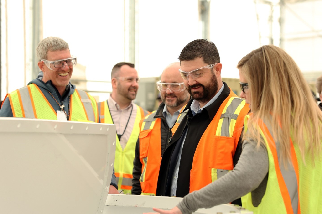 An EM leader in an orange safety vest observes what is in front of him while others stand around him and talk