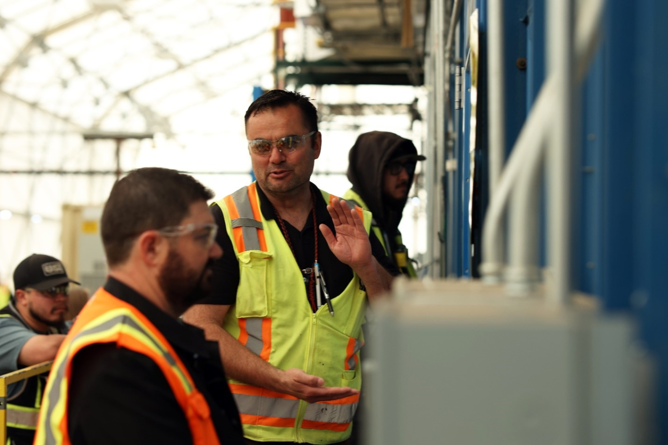 Two men wearing safety vests and gear speak to each other