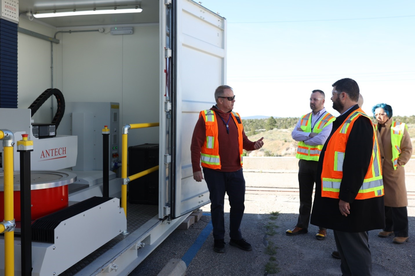 A group of people in safety vests stand around a truck with its door open and look at canisters inside