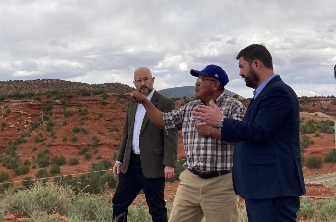 Three men stand in a hilly area a speak to each other