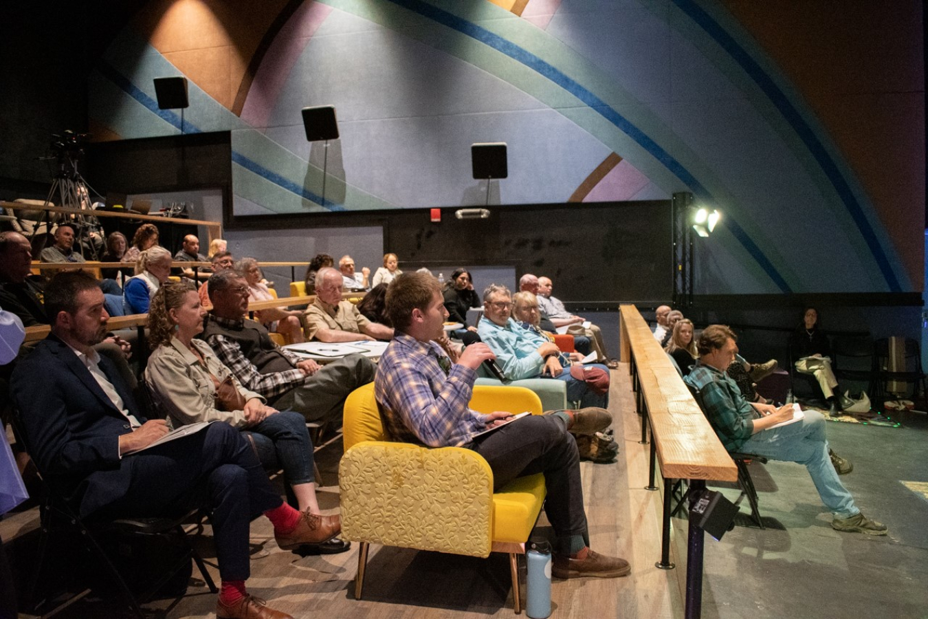 A side view of an audience in an auditorium sitting in seats listening to the speakers