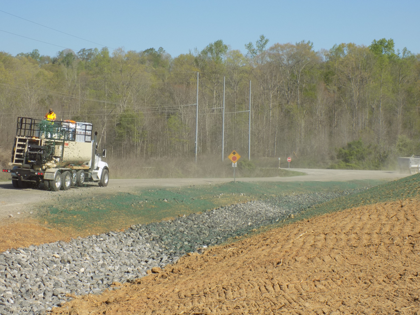 A construction truck drives on a gravel road beside a dirt hill