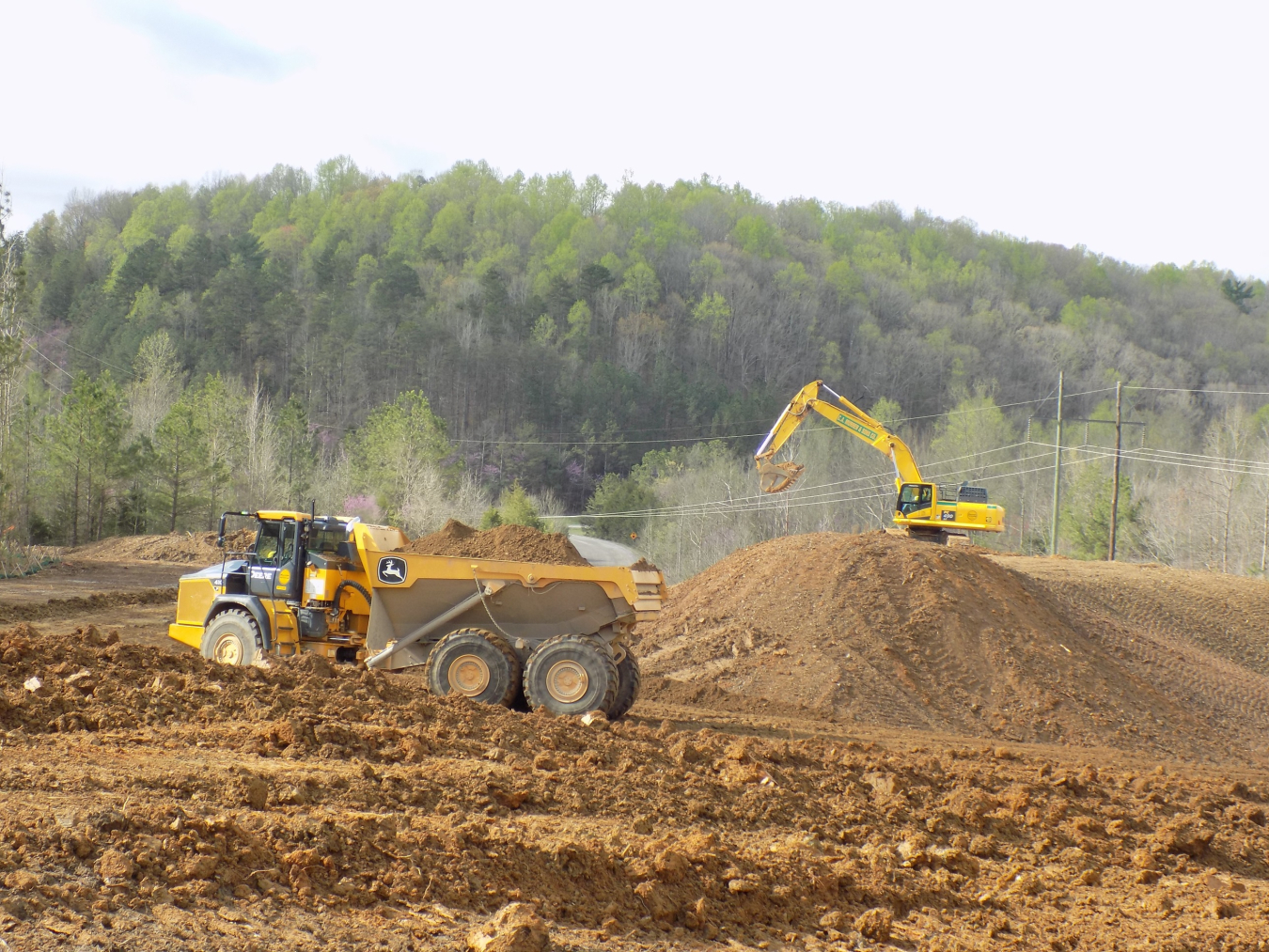 A dirt field with two yellow construction vehicles working 