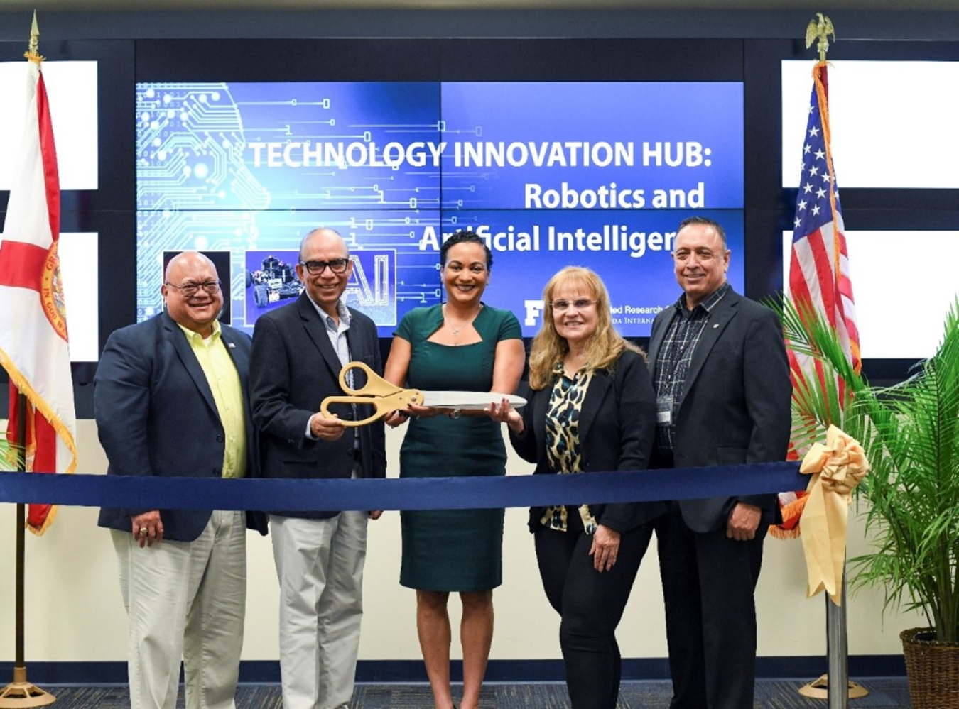 A group of people stand at the front of a room and pose for a picture before performing  a ribbon cutting ceremony