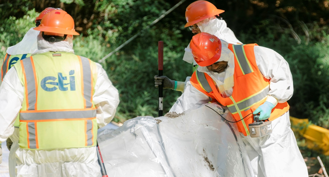 Three men in safety gear work on a white tube