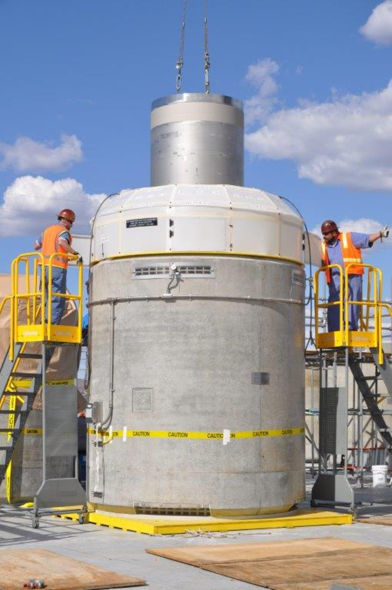 A large metal and concrete tank with two workers on ladders on either side of it