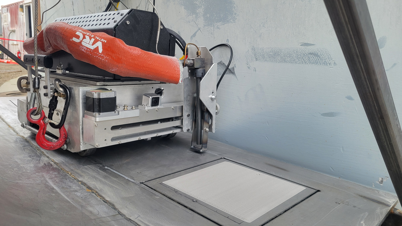 A metal and orange robot machine applying metal patches to the side of an outside building wall