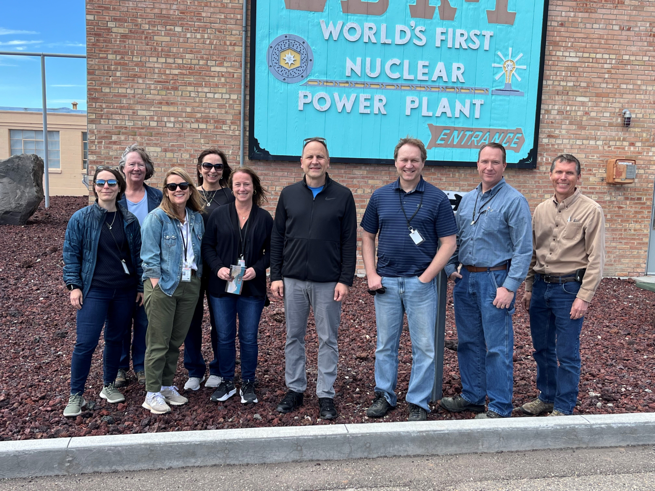 A group of people stand outside a brick building and pose for a group picture
