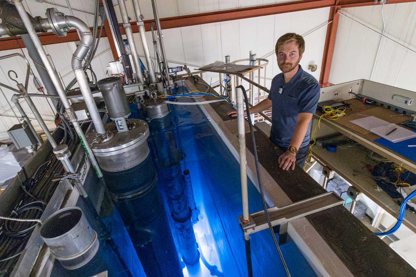 Man in blue shirt stands next to glowing blue reactor pool