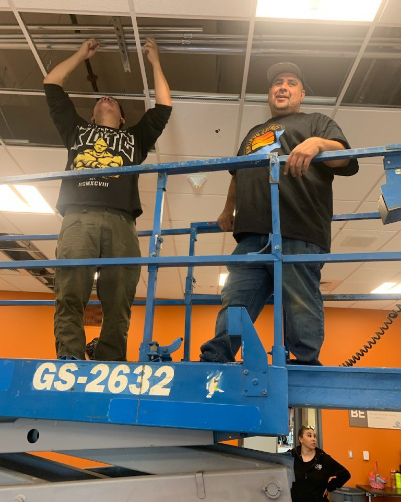 Two men on scissor lift installing indoor lighting.