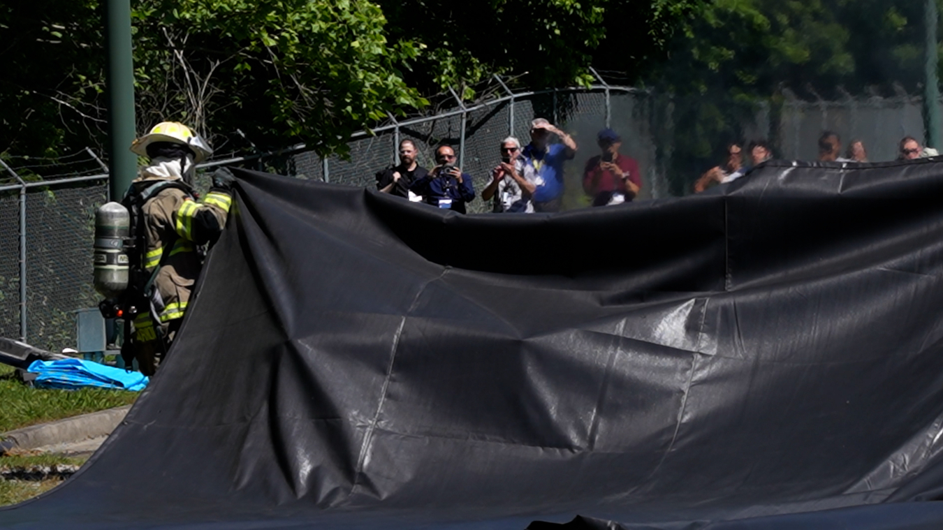 A firefighter in full gear pulls a large black fire blanket over the ground