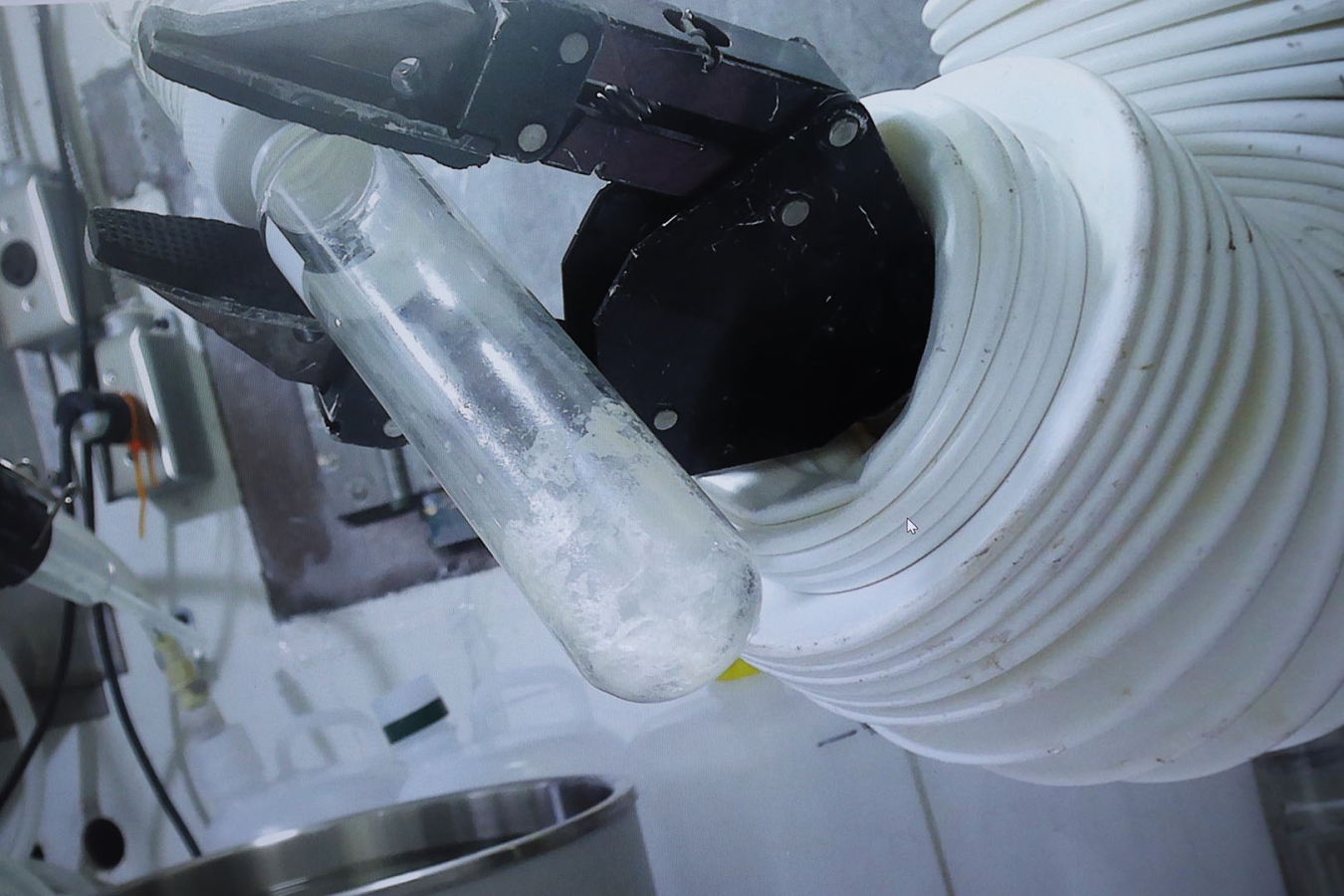 An up close shot of a machine's arm holding a test tube with a clear crystal substance inside