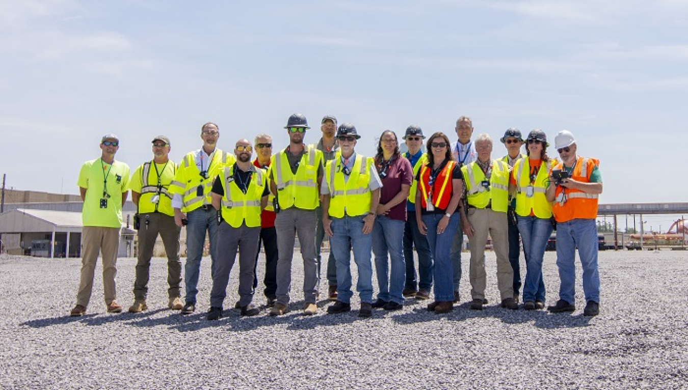 A group of employees pose for a group picture outside wearing yellow and orange safety vests