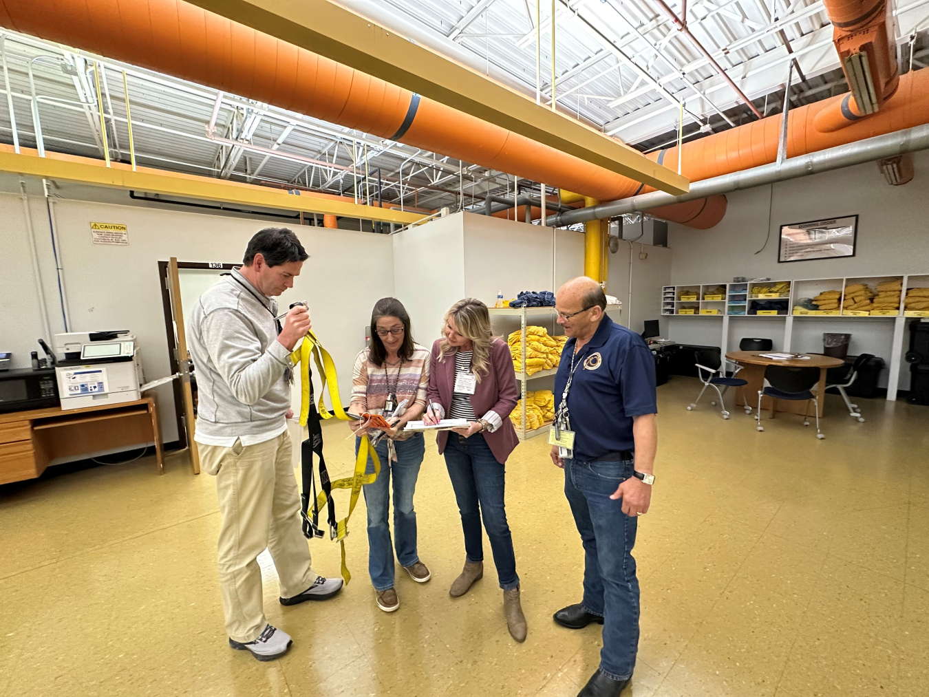 A group of four people stand inside a training facility room and look at a piece of paper together