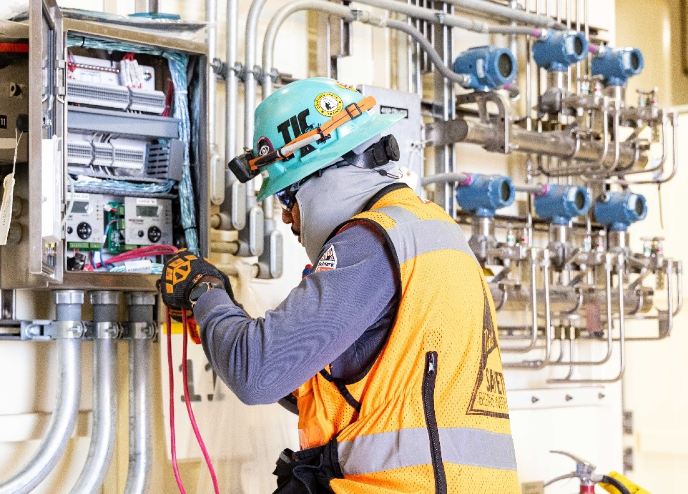 A man in a blue hard hat and orange works on a control panel