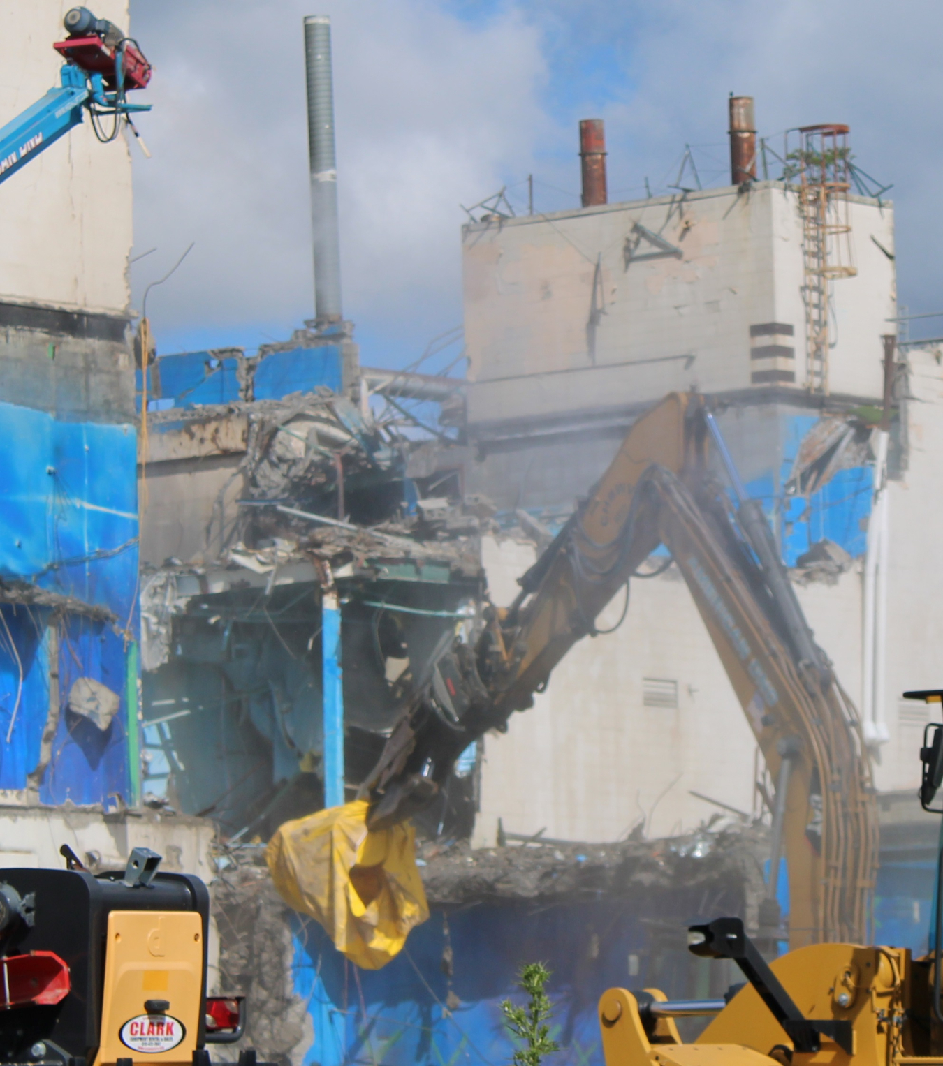 A large crane demolishes a blue, white, and grey building
