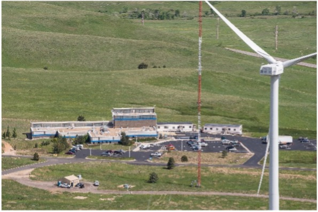 Wind turbine stands in front of campus with grassy hill in the background.