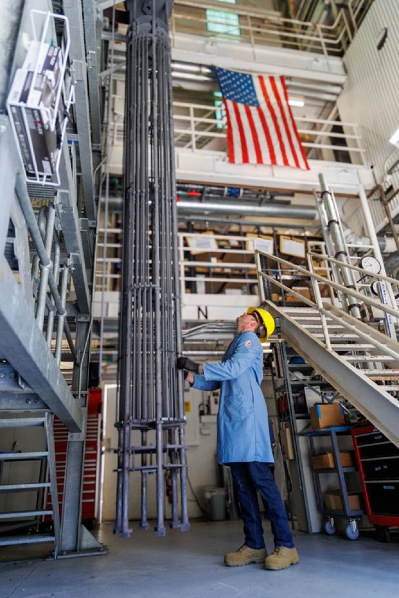 An engineer inspects 12-foot SiGA cladding rods with an American flag hanging in the background.
