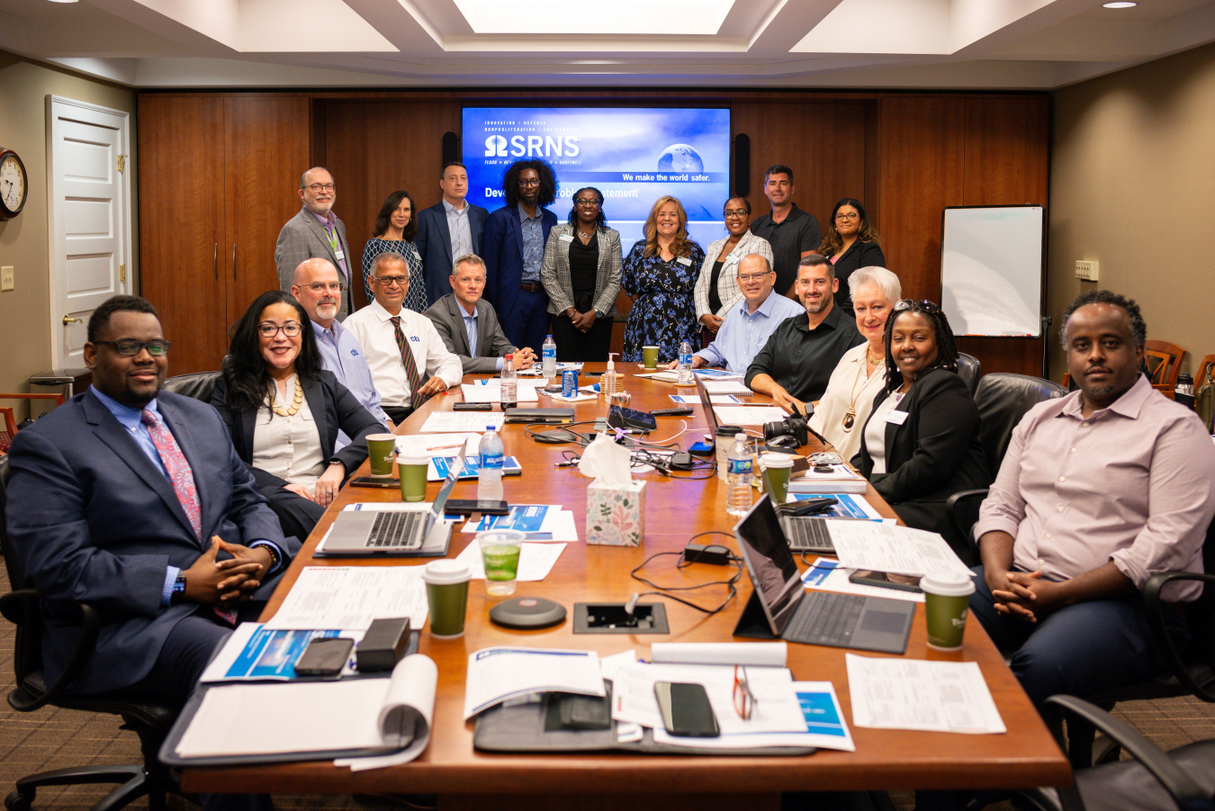 A group of professionals sit and stand around a large table in a conference room