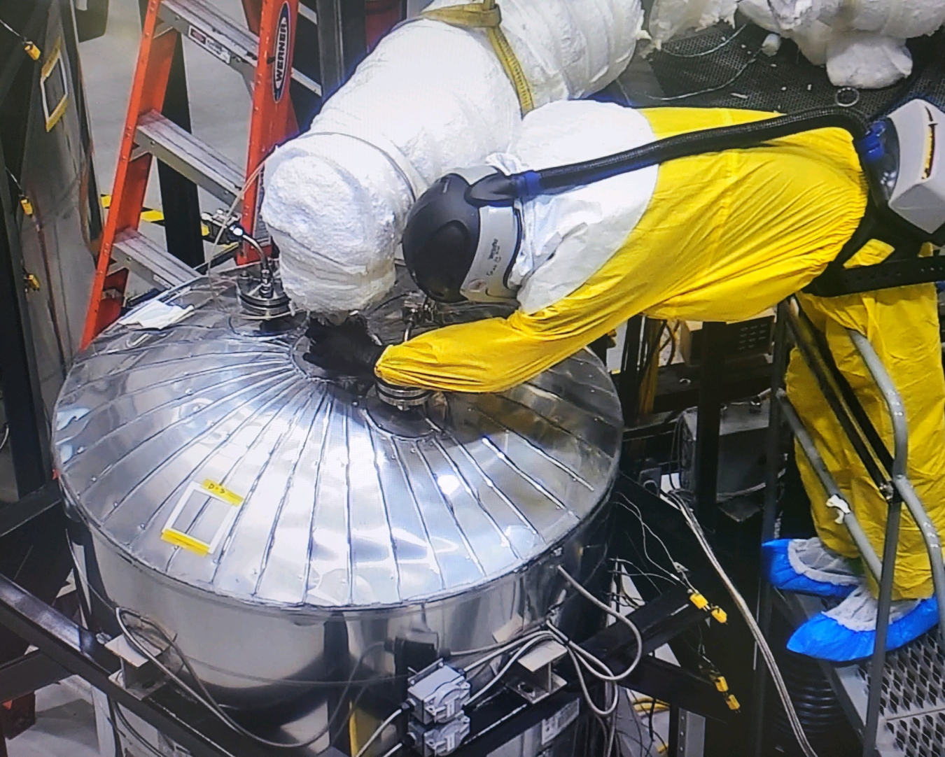 Worker in yellow hazmat suit connects a tube to a metal chamber