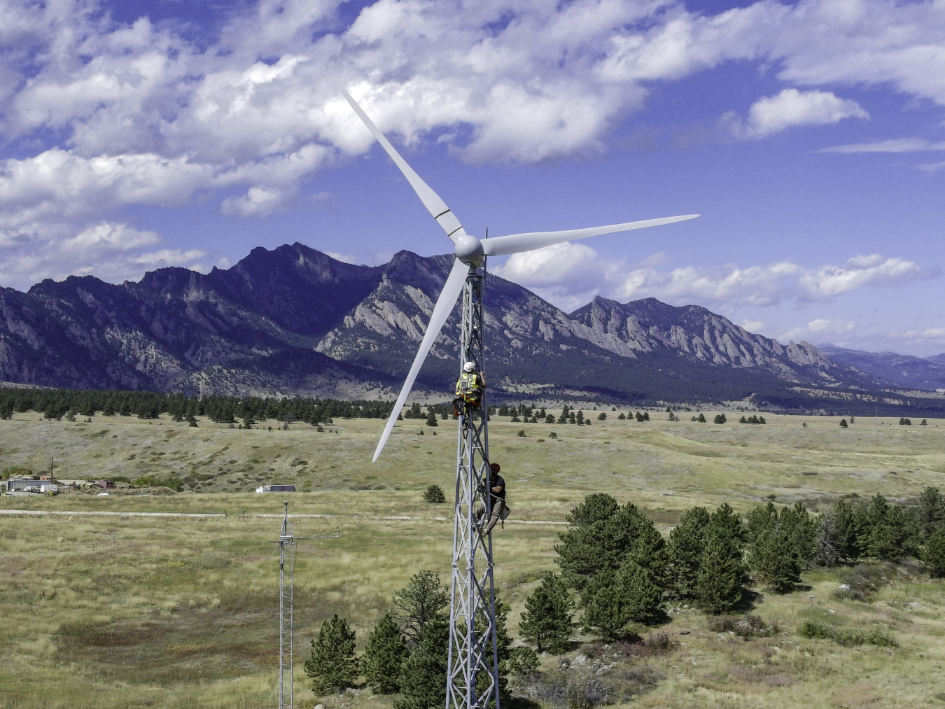 Two workers on a wind turbine with lattice tower construction.  