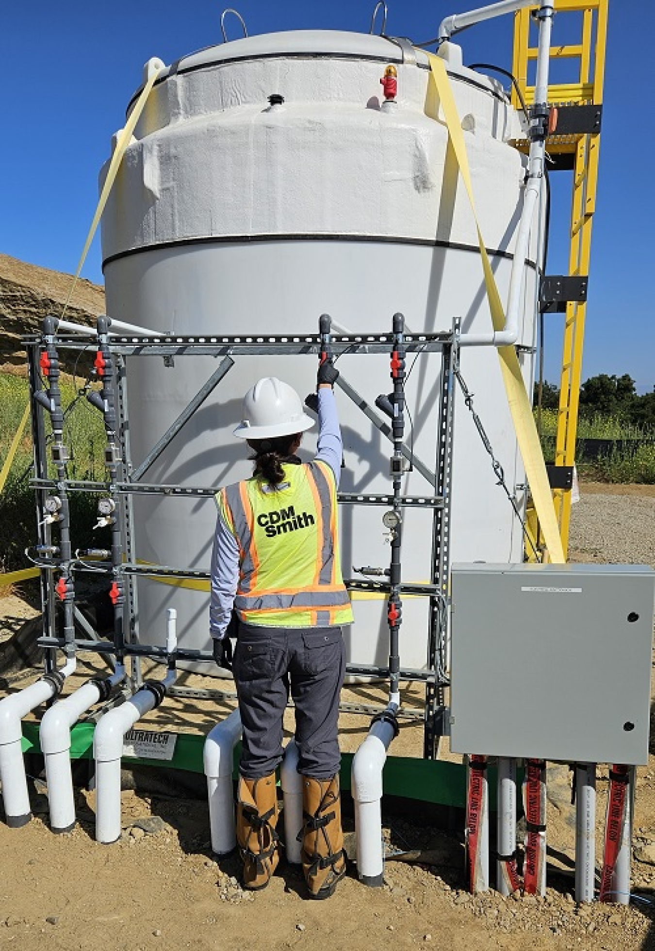A worker adjusts a ball valve on piping manifold on a groundwater storage tank.