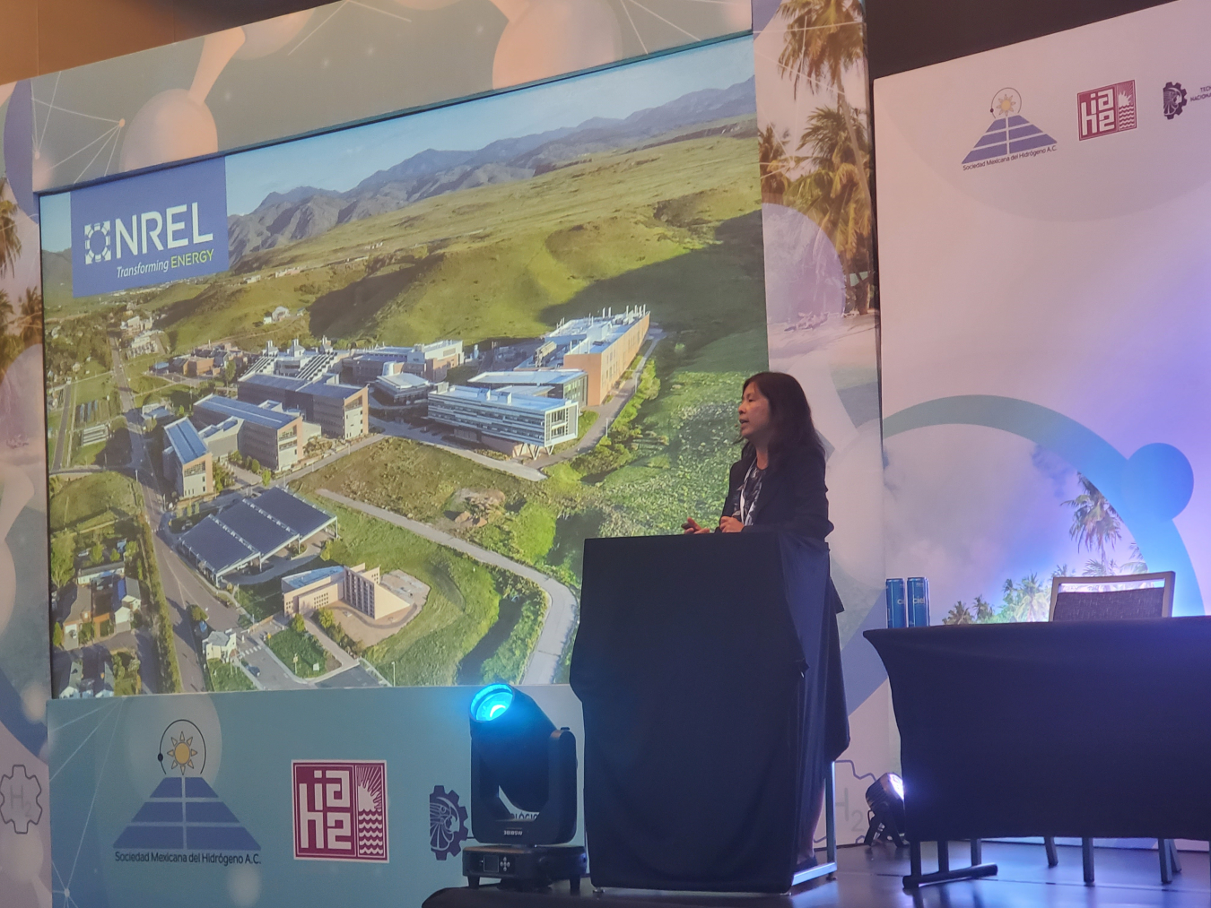 Huyen Dinh delivers a plenary talk at a podium with a presentation behind her labeled "NREL."