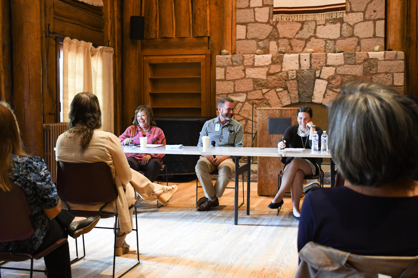 A group of people sit at a table at the front of a room, the speak to each other and the audience