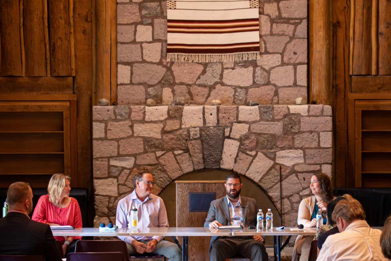 Four people sit at a table at the front of a room and speak to an audience